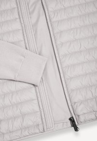 Světlá šedá prošívaná bunda s horizontálním prošitím, otevřeným předním zipem a viditelným žebrovaným úpletovým lemem rukávu.