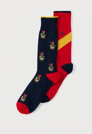 Une chaussette marine avec des orteils rouges et de petits motifs d'ours en peluche, et une chaussette rouge avec une bande diagonale jaune et un logo de joueur de polo vert.