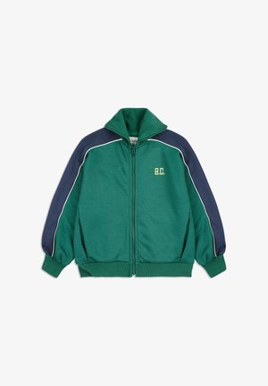 Zeleni dukserica s patentnim zatvaračem, visokim ovratnikom, tamnoplave ramena, bijelim detaljima i izvezenim logom "B.C." u žutoj boji.