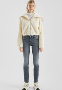Cremfarbene, flauschige Zip-Up-Jacke mit einem breiten Kragen, kombiniert mit schmal geschnittenen grauen Jeans und weißen Sneakers.