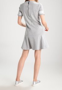 Grå klänning med kort ärm och utsvängd nederdel, med en dragkedja i ryggen. Accentuerad med en logotyp på ärmen. Bärs med silverfärgade sneakers.