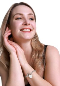 Bracciale in argento con charm a forma di cuore, caratterizzato da un design a catena collegata. Texture liscia, finitura lucida su uno sfondo neutro.