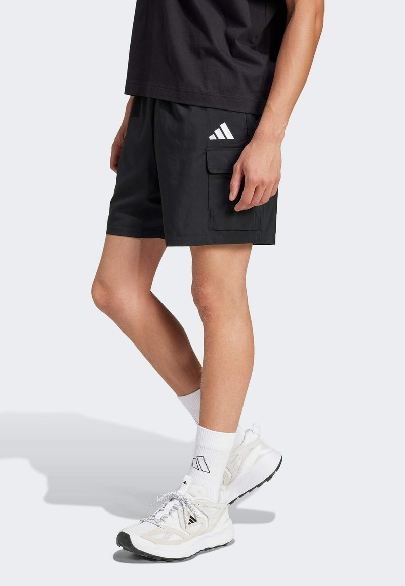 Black cargo shorts with a side pocket, featuring a white Adidas logo on the upper left. Paired with white socks and light sneakers.