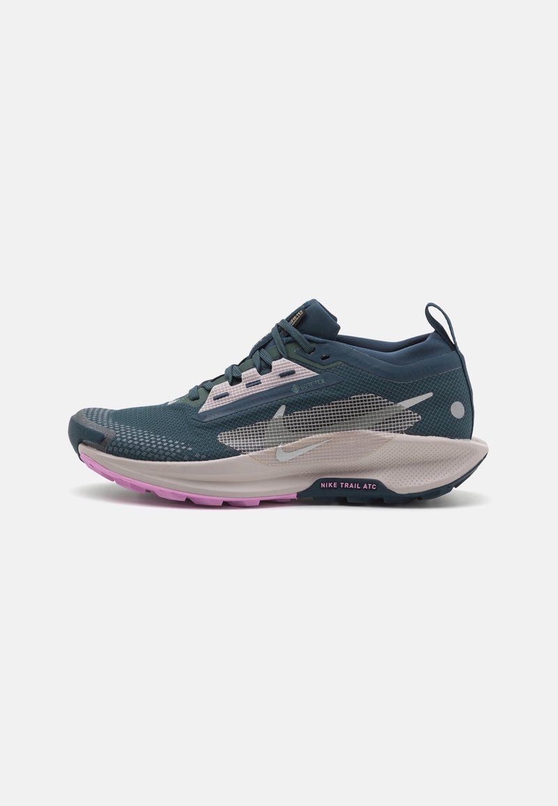 Chaussure de trail running Nike bleu sarcelle foncé et rose avec dessus en mesh, semelle blanche épaisse et lacets noirs sur fond uni.
