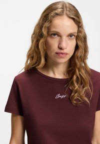 Μπορντό κοντομάνικο μπλουζάκι με στρογγυλή λαιμόκοψη και κεντημένο λευκό λογότυπο "Boss" στο στήθος. Μαλακό βαμβακερό υλικό, casual εφαρμογή.