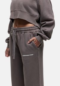 Grijze cropped sweatshirt en bijpassende joggingbroek van zachte stof. De broek heeft een elastische tailleband en een wit logo-detail op de dij.