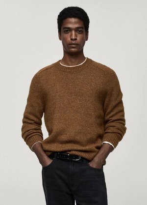 Brown knit sweater with ribbed cuffs and crew neckline, featuring contrasting white interior at the collar. Paired with dark jeans.
