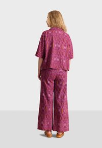 Twee-delige outfit bestaande uit een kortlopende, loszittende top en een broek met wijde pijpen, beide in een levendig roze patroon met geometrische ontwerpen.
