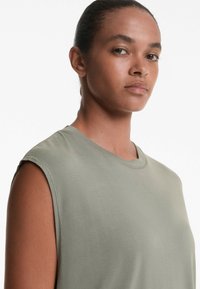Ärmlös topp i ljus olivgrön färg tillverkad av mjukt tyg. Har rund halsringning och en slät struktur, med minimala sömmar och inga utsmyckningar.