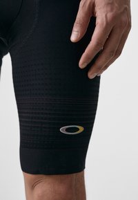 Shorts atletici negri cu un model texturat, un design apropiat de corp și un logo accentuat pe piciorul inferior.