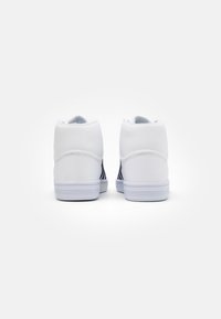 Baskets montantes blanches au design épuré, avec une texture lisse, un col rembourré et des accents noirs contrastants sur les côtés.