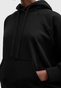 Black hooded sweatshirt made of cotton blend fabric, featuring a front pocket, drawstrings, and raglan sleeves. Smooth texture and relaxed fit.