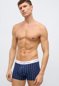 Marineblaue Boxershorts mit weißem geometrischem Muster und einem weißen Bund mit dem "Tommy Hilfiger"-Logo. Eng anliegendes Design, dehnbares Material.