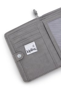 Portafoglio RFID-safe grigio con texture in tessuto, dotato di più scomparti per carte, una tasca trasparente per l'ID e un'etichetta con il logo Kipling all'interno.