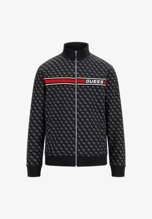 Veste zippée noire avec un motif répétitif, col montant, rayure horizontale rouge et blanche, et logo "GUESS" en blanc.