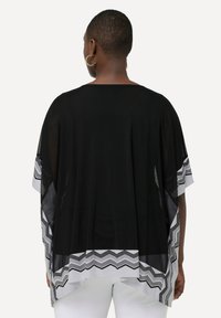 Kimono nero con tessuto trasparente e motivo a zigzag bianco all'orlo. Vestibilità ampia con maniche corte, progettato per un facile sovrapposizione.