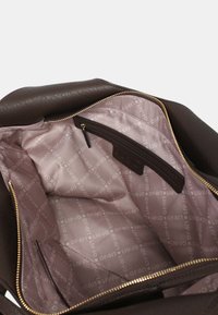 Sac à main en cuir marron ouvert pour montrer un intérieur en tissu rose clair avec le logo "Liu Jo" répété et une poche zippée intérieure.