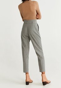 Bruine ribgebreide trui, grijze geruite pantalon met een tailored fit, en beige enkellaarsjes met blokhakken. Casual, stijlvolle outfit.
