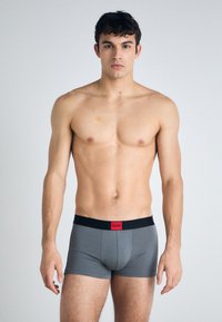 Graue Boxer-Briefs mit schwarzem Bund und rotem Logo. Glattes, enganliegendes Design, mittlere Leibhöhe und weiche Textur.