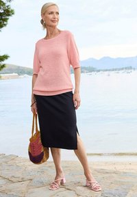 Lichtroze gebreid sweater met korte mouwen, gecombineerd met een zwarte midi rok, roze blokhak sandalen en een multicolor geweven tas.