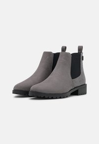 Un paio di stivaletti alla caviglia grigi in suede con pannelli elastici neri ai lati e retro testurizzato, tacco basso a block e linguette per il trasporto su uno sfondo bianco.