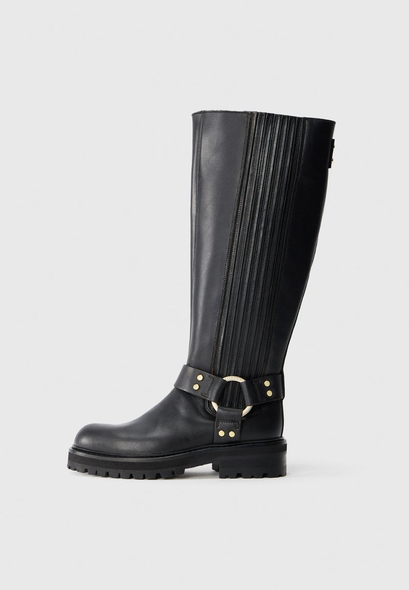 Bota de cuero negra hasta la rodilla con ribete elástico, suela de taqueado y correa decorativa con anillo de metal dorado y remaches.