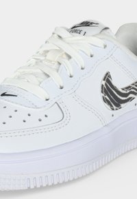 Λευκό αθλητικό παπούτσι Nike Air Force 1 με λευκά κορδόνια και ένα λογότυπο Nike Swoosh σε σχέδιο ζέβρας σε μαύρο και άσπρο στην πλευρά.
