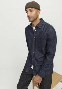 Camicia di jeans blu scuro con chiusura a bottoni, una tasca sul petto e bottoni bianchi; presenta un accento rosso sull'orlo.