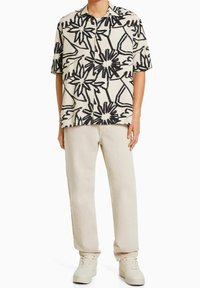 Kratký rukáv košile v krémové látce s černým abstraktním květinovým vzorem; v kombinaci s béžovými kalhotami a bílými teniskami. Má design na knoflíky.