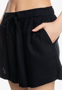 Sorte linshorts med elastisk midje og snøring. Har sidelommer og en avslappet passform, med en jevn tekstur.