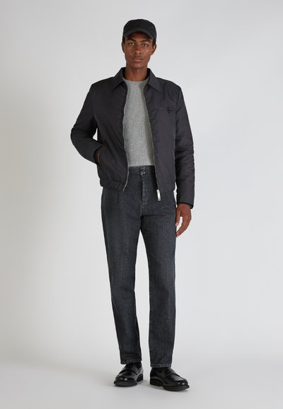 Schwarze Bomberjacke mit einem silbernen Reißverschluss, grauem Rippenpullover, dunklen Jeans und schwarzen Schuhen. Einfaches Design ohne sichtbare Muster.