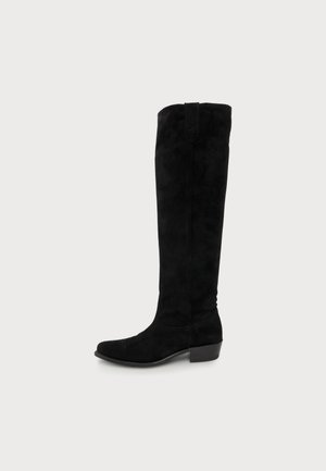 Botte noire en daim montant jusqu’au genou, avec un talon bloc bas, présentée de profil sur un fond uni.