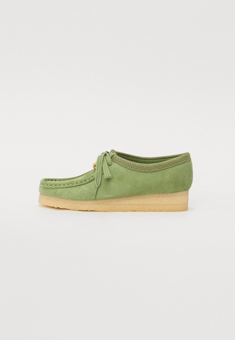 Chaussure en daim verte avec un bout arrondi, des détails cousus, un lacet noué à l'avant et une semelle en caoutchouc beige.