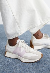 Baskets New Balance avec un upper en mesh blanc, des accents en daim rose, des superpositions en daim gris et une semelle extérieure en caoutchouc texturé.