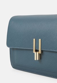 Borsa a tracolla blu con texture, dotata di chiusura a patta e dettagli in metallo dorato. Il materiale presenta un sottile motivo a rete incrociata.