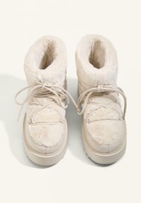 Cream-colored fur-lined boots with a textured surface, featuring a sturdy sole and decorative laces for closure.