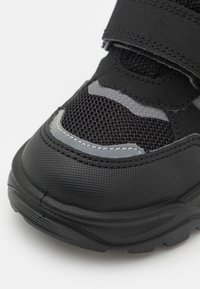 Schwarzer Sportschuh mit strukturiertem Obermaterial, Mesh-Elementen und grauen Akzenten. Verfügt über eine robuste Gummisohle und verstellbare Klettverschlüsse.