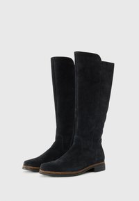 Bottes en suede noires jusqu'aux genoux avec un talon plat, texture lisse et couture marron contrastante le long de la semelle. Détail de fermeture éclair sur le côté.