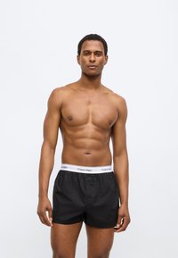 Μαύρα εσώρουχα μποξέρ με λευκή ζώνη μέσης που φέρει το λογότυπο "Calvin Klein". Κατασκευασμένα από ελαφρύ ύφασμα, με άνετη εφαρμογή και λεία υφή.