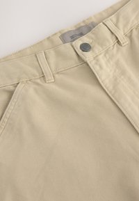 Beige cotton trousers with a classic design, featuring a metal button, belt loops, and stitched accents at the waist and pockets.