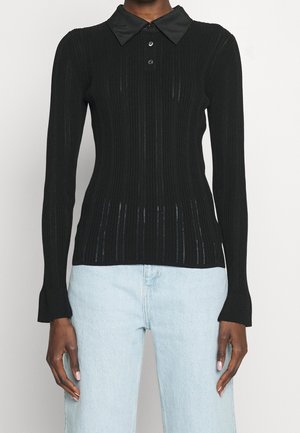 Femme portant un haut noir côtelé à manches longues ajusté avec un large col et trois boutons, associé à un jean taille haute bleu clair.