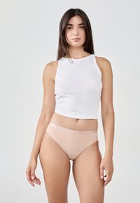 Lekki biały bawełniany top na ramiączkach o skróconym kroju, w połączeniu z jasnoróżowymi bezszwami majtkami z subtelną, błyszczącą gumką. 