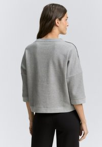 Grauer, kurzer Pullover mit einem strukturierten Strickmuster, weiten Ärmeln und einem schlichten runden Ausschnitt, kombiniert mit schwarzen Hosen.