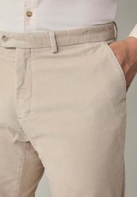 Bež korduri hlače s diskretnom rebrastom teksturom. Imaju standardni pojas, prednje džepove i skriveno kopčanje na dugme.