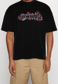 Sort kortærmet t-shirt med farverigt graffiti-inspireret logo på brystet. Fremstillet af bomuldsmateriale, afslappet pasform og rund halsudskæring.