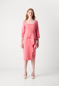 Robe rose, longueur genoux, en tissu lisse. Présente un décolleté carré, des manches trois quarts et un détail de volants asymétriques.