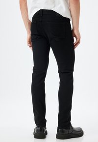 Jeans negros de corte slim con una textura suave, que cuentan con dos bolsillos traseros y una cintura estándar, combinados con calzado negro.