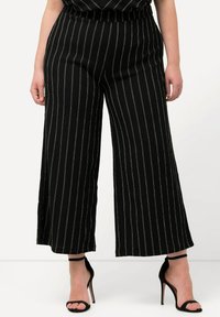 Pantalon large noir avec des rayures blanches verticales, en tissu texturé, et une taille élastique. Assorti à des sandales à talons hauts noires.