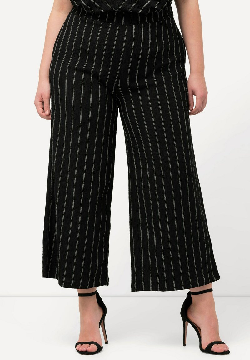 Pantalon large noir avec des rayures blanches verticales, en tissu texturé, et une taille élastique. Assorti à des sandales à talons hauts noires.