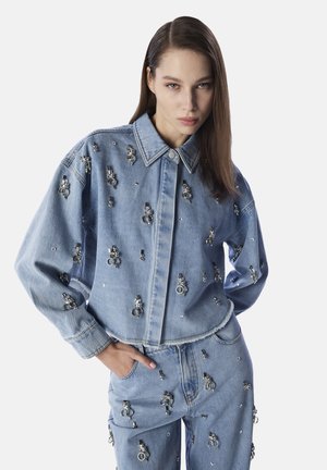 Giacca di denim azzurro chiaro con abbellimenti metallici e collo classico. Il design include tasche oversize e un orlo corto.